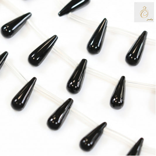 Black agate teardrop beads 6x16mm scattered on white background showing natural stone texture and glossy finish